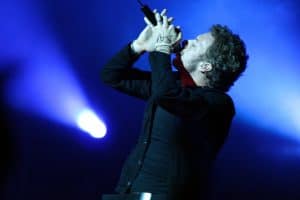 Chris Martin singing on stage with a blue background