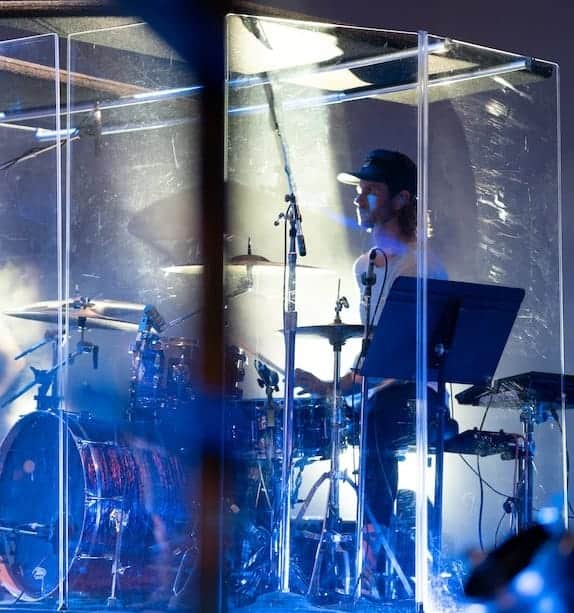 drummer playing in a glass cage with music stand