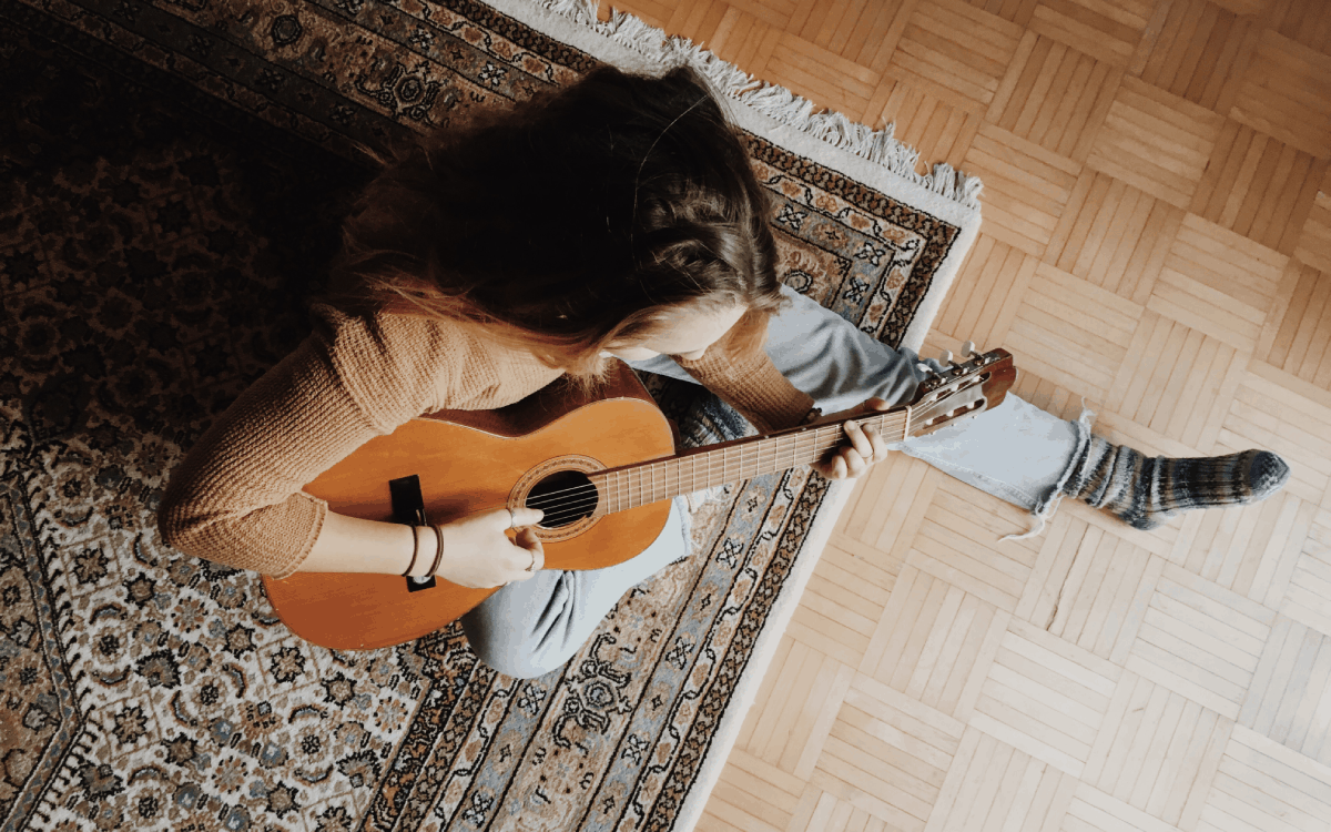 Lady playing classical guitar sitting on a rug