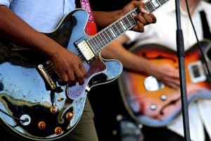 Guitar care tip showing people playing semi-acoustic guitars on stage